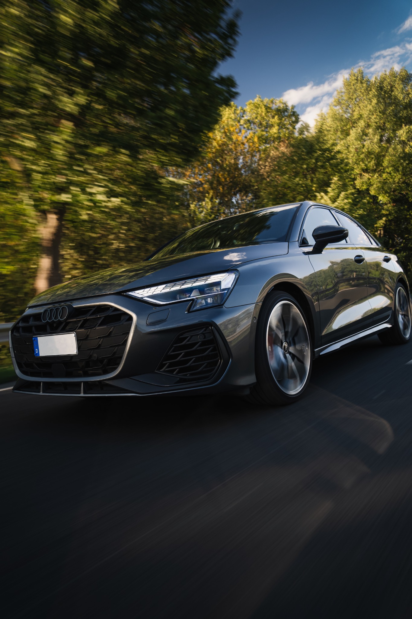 Grauer Audi S3 während der Fahrt vor verwischten Bäumen