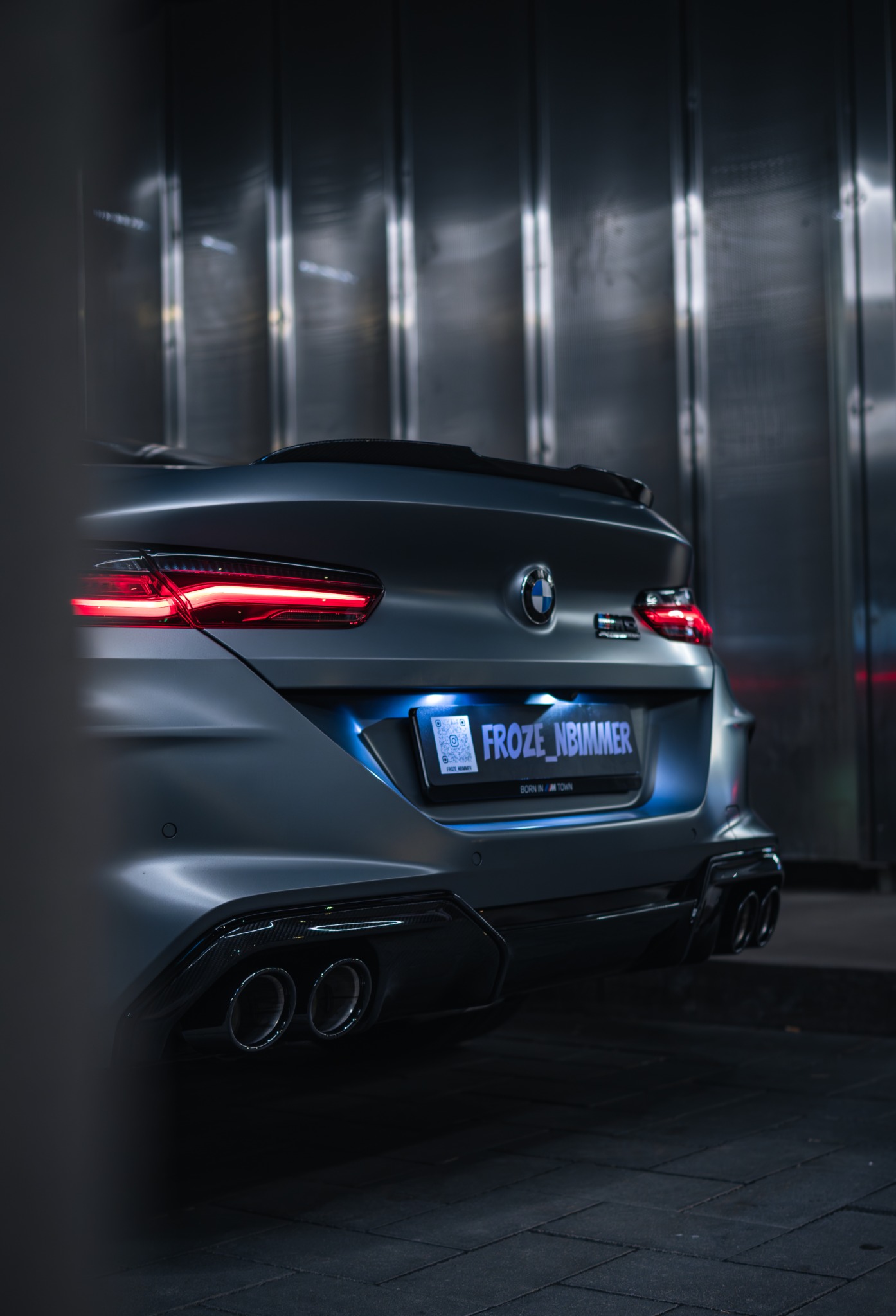 BMW M8 von hinten mit roten Rückleuchten vor einer Metallfassade